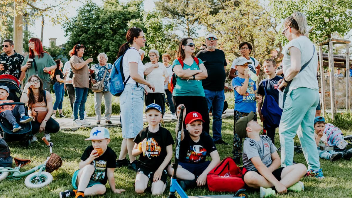 A diverse group of families and children enjoying an outdoor event on a sunny day in a park setting.