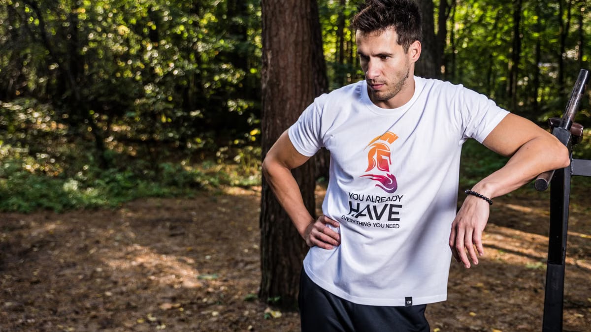 Man in forest wearing casual t-shirt, resting during outdoor workout.